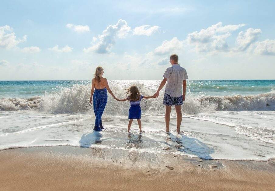 man, woman and child holding hands on seashore