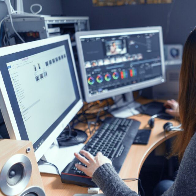 a woman sitting at a desk with two computer monitors